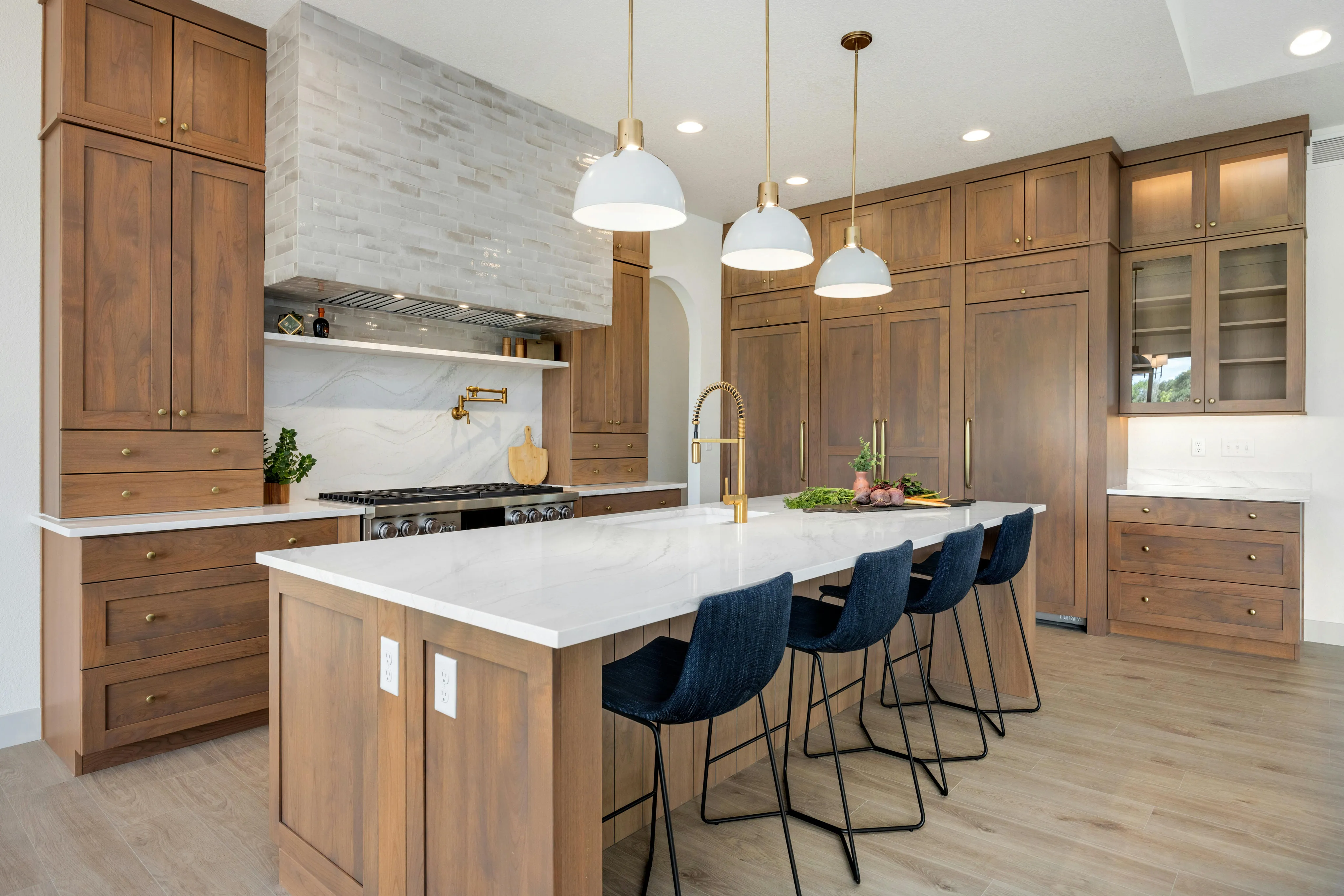 Bright modern farmhouse kitchen with walnut cabinetry, a white-quartz island, and navy bar stools